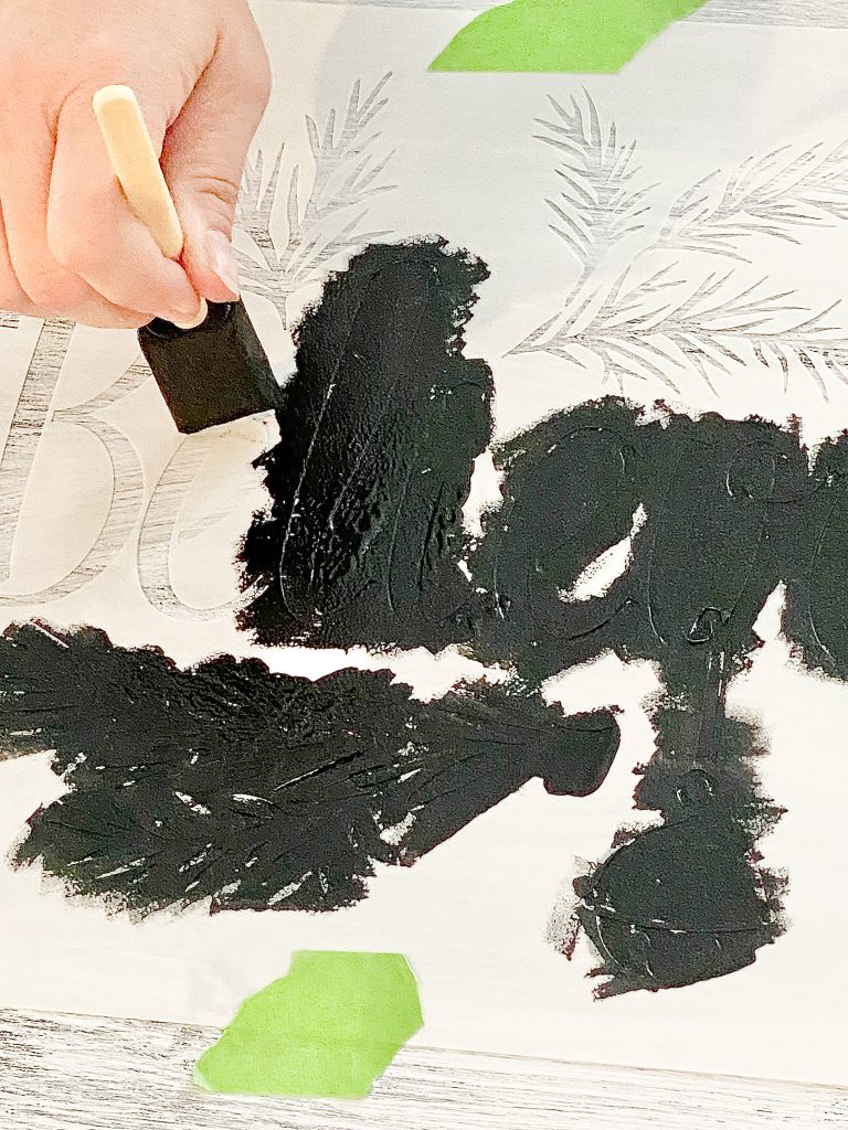 Hand holding foam brush painting black paint on stencil. 