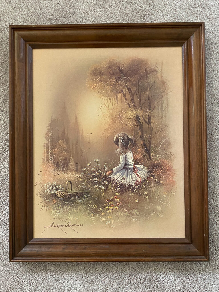 Painting with a brown frame of a little girl sitting in a field of flowers. 