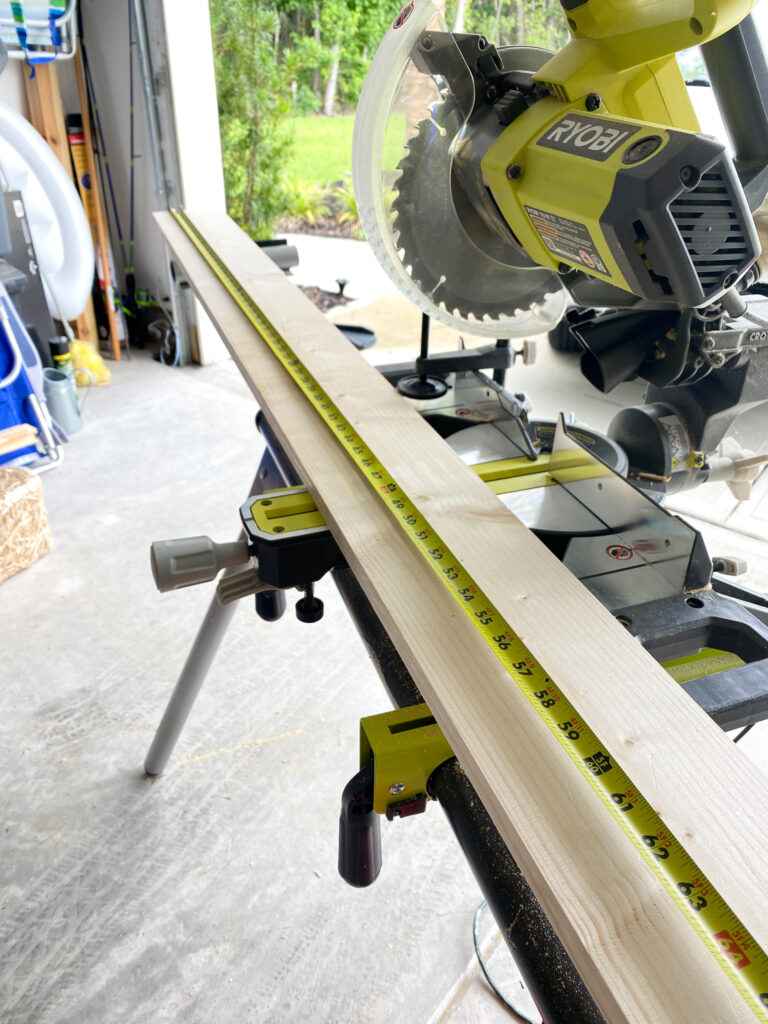 Sliding miter saw on a stand with a piece of wood laying across to be cut and a measuring tape across the piece of wood. 