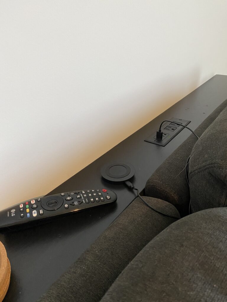 Close up of the sofa table behind the gray sofa showing a remote, coasters, and charging port. 