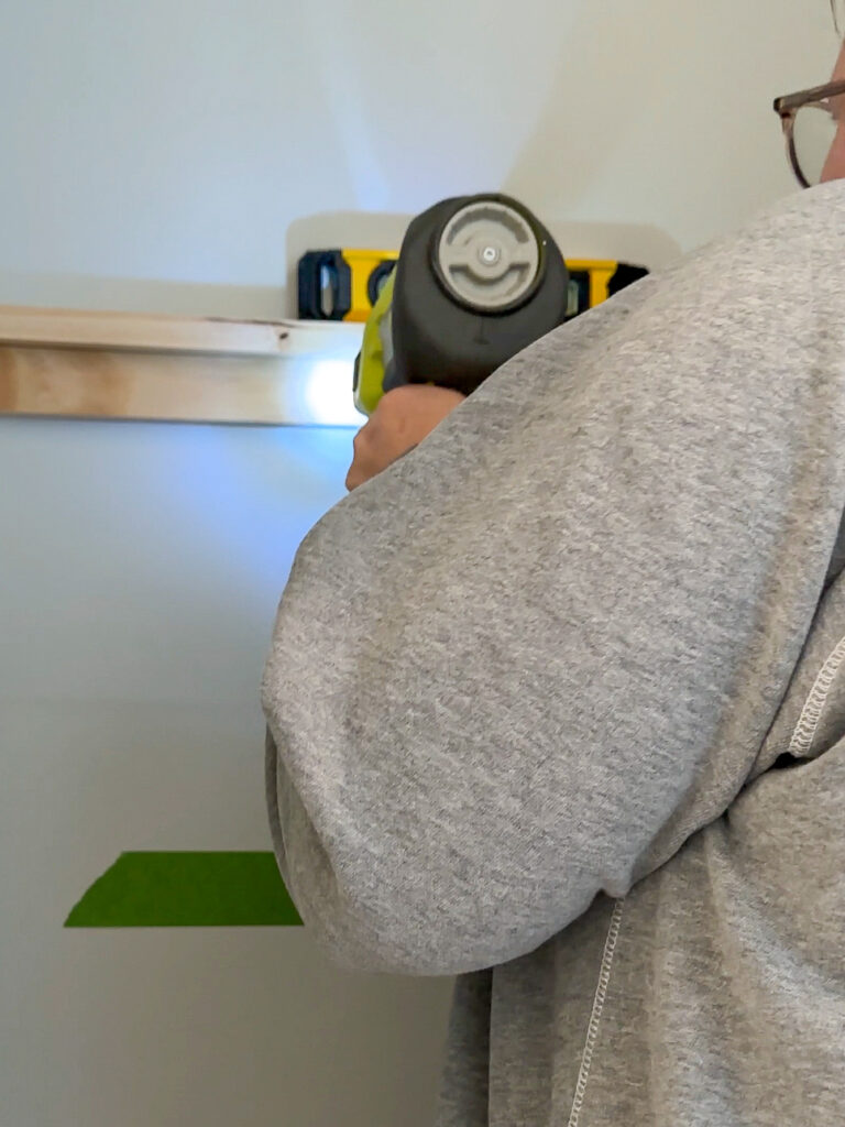 Using a brad nailer to secure a support piece to the wall. 