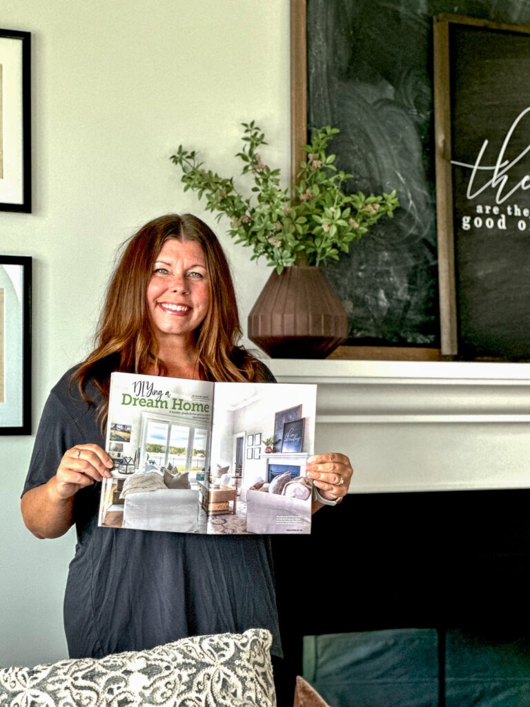 Brooke Cribbs holding a magazine open standing in front of a fireplace, the same one pictured in the magazine.